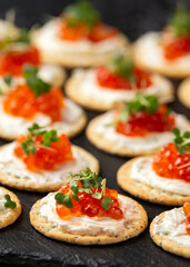 Salmon caviar and soft cheese savory crackers with sesame and poppy seeds served on black slate board