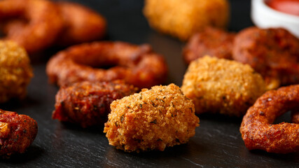 Fried Buffalo onion rings, tater tots and sweetcorn fritters with ketchup on rustic stone board. Party take away food