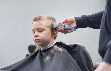 the process of cutting a blond boy with a long braid in a chair in a barbershop salon, a barbershop...
