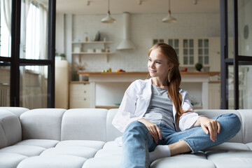Smiling woman sitting on sofa at home, enjoying lazy weekend alone in own apartment.