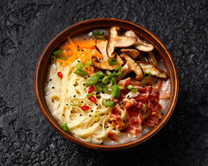 Pork bone Japanese style ramen noodle soup with crispy bacon, shiitake mushrooms and spring onions in clay bowl