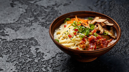 Pork bone Japanese style ramen noodle soup with crispy bacon, shiitake mushrooms and spring onions in clay bowl
