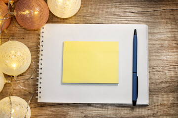 A Notepad with a sheet of notes is on the wooden table near the Christmas garland. Christmas background with space for text