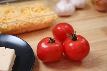 A set of fresh vegetables on a wooden kitchen table for cooking. Onions, garlic, red tomato and cheese on the table.