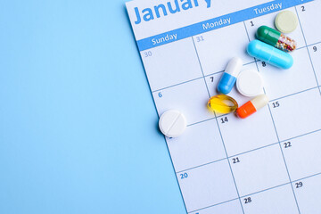 Colorful pills and capsules on calendar on light blue background. Prescription, dosage, organizer...