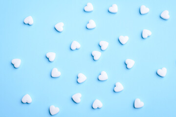 Small, white sweet pill in a heart shape on light blue background. Treatment, vitamins concept.