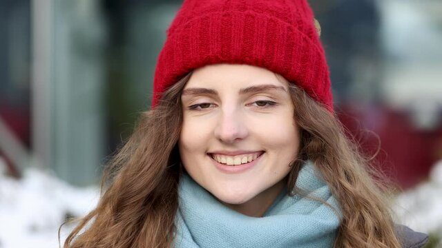 Portrait young attractive curly haired smile woman with red hat look at camera at city center feel happy. Fshion girl. Stand on street. Cute face. CLose up