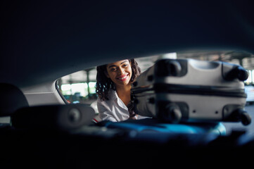 Smiling woman puts suitcases into the car, parking