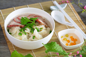 Shrimp wonton with red pork in soup on bamboo mat and wooden table