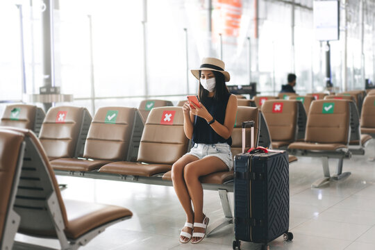 Young adult tourist woman wear mask for virus outbreak at airport terminal with social distancing chair.