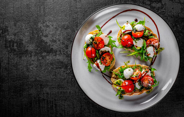 Italian bruschetta with roasted tomatoes, mozzarella cheese, balsamic vinegar and herbs on plate