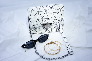 Women handbag with black sunglasses on a white background. Leather bag on a gathered fabric. Side...