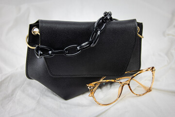 Women handbag with black sunglasses on a white background. Leather bag on a gathered fabric. Side...