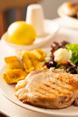 Fried pork entrecote on the bone with stewed pumpkin pieces and salad in a plate close up, green salad with cauliflower and napa cabbage, bell pepper and spices