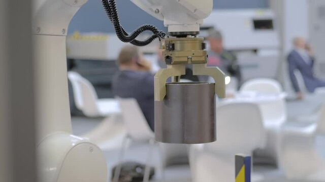 Pick and place industrial robotic clamp arm manipulator moving cylindrical metal workpiece at modern robot exhibition, trade show - close up view. Manufacturing, engineering, ai, technology concept