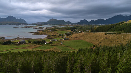 Beautiful panoramic view of the west of Vestvågøy island, Lofoten, Norway with fjord Buksnesfjorden, Leknes town, rough mountains, agricultural fields and forest of coniferous trees in foreground.