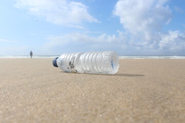 Climate change. Close-up of a bottle on the beach and a man walking in the background - pollution waste sea and sand