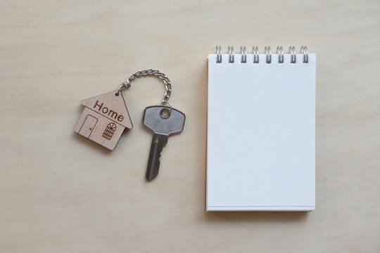 Home key with house keyring, pencil, note book on wooden table