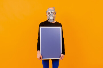 Funny strange man in respirator posing with a board  over orange background