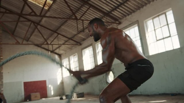 Fitness man workout with battle ropes inside abandoned warehouse with personal trainer. Muscular man doing battle rope workout with instructor.
