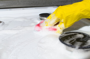 Woman's hand in glove cleaning gas stove with sponge with foam. Copious foam from chemical cleaning fluid.
