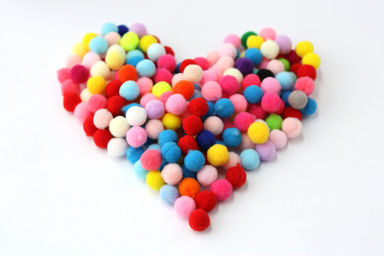 Fur colorful balls in the shape of a heart on a white background. Fluffy pom-poms for decoration and needlework. Selective focus.