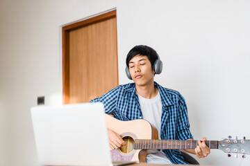Pre teens boy 15 years play guitar worship.Live streaming video.Online learning music.Lockdown at home.Influencer asian handsome teenager boy practice guitar.Technology, Online, Macbook, Apple brand.
