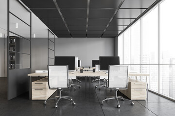 Grey office room with armchairs and computers on the tables near window