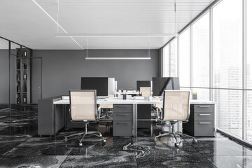 Dark grey office room with armchairs and computers on the tables near window