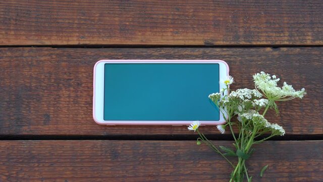 Closeup top view flatlay 4k video of modern smartphone laying on brown wooden surface. Screen of device with empty blank blue color.