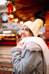 Beautiful woman enjoys winter holidays walking on Christmas market. Young woman posing on  festive street. New year.