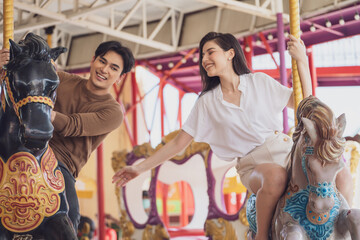 Fototapeta na wymiar couple asian man and woman dating and riding on horse at Carousel amusement park. Concept happy and lovely life of teenager.