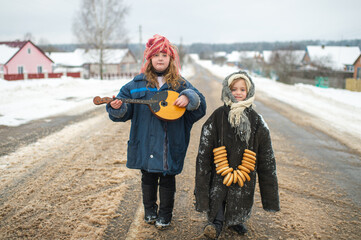 Two beautiful village girls stand on the road with balalaika and barankas in winter
