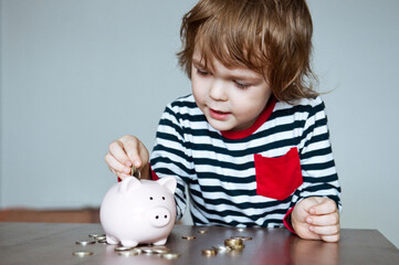 Cute baby preschooler puts money in the piggy Bank.