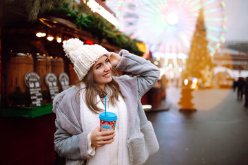 Happy woman  drinking hot coffee in Festive Christmas fair. Beautiful woman enjoys winter holidays on Christmas market. New year.Lights around.