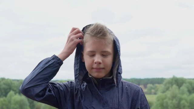 Young happy kid standing under pouring rain in beautiful scenic nature landscape.