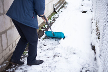 A man in a blue jacket cleans the path from the snow near the house