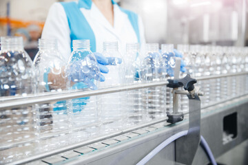 Female worker holds transparent plastic bottle background of automated dairy production line