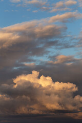 Sunset sky. Big white fluffy storm cumulus clouds in yellow orange sunlight on blue sky background texture