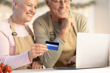 Elderly Couple Using Credit Card And Laptop Buying Groceries Indoors