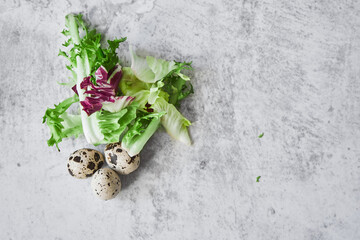 Ingredients for cooking. Three quail eggs and lettuce leaves on a gray concrete background. Healthy food for getting vitamins to strengthen immunity. Healthy lifestyle, cooking concept.
