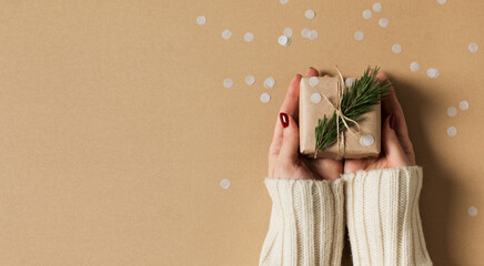 Womans hand in white sweater with kraft paper gift box on brown background, christmas, holidays and eco theme