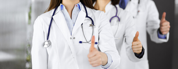 Group of doctors standing as a team with thumbs up in sunny clinic. Good news and Hope for a cure. Medicine concept during Coronavirus pandemic. Covid-2019