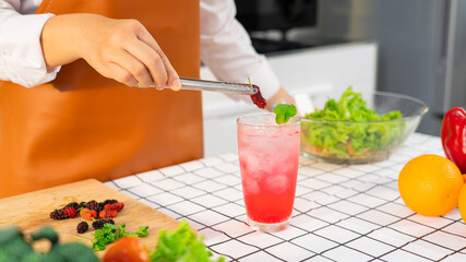 Women hands prepairing mocktail by putting sweet mulberry into a glass with an iced pink color drink.