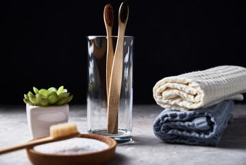 Bamboo toothbrushes in glass and bathroom towels on dark background