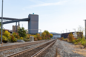 Fototapeta na wymiar Train tracks running alongside a steel mill industrial complex, fall season with blue and cloudy skies, horizontal aspect