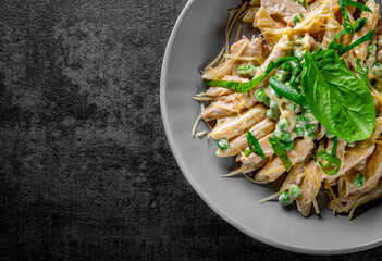Penne pasta with chicken meat, cream sauce and cheese in a bowl on Dark grey black slate background