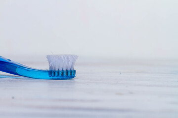 A blue toothbrush with a bad old bent bristles rests on a white wooden surface.