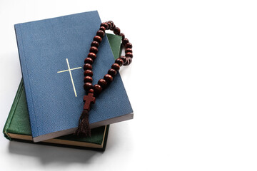 Religious literature and freedom of religion. Brown wooden rosary on religious books stack with closed bible with Christian cross on book cover against white background with space for text. Copy space