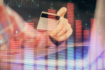 Double exposure of man hands holding a credit card and Forex graph drawing. Stock trading and digital fintech in Internet E-commerce concept.